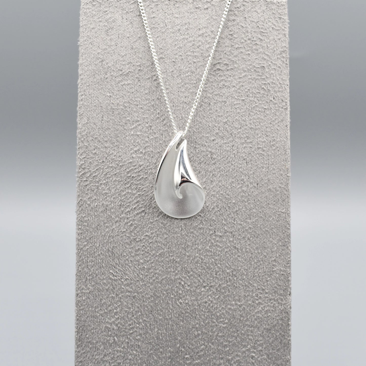 A curved pendant with a twist in a matt and polished silver finish on a silver chain