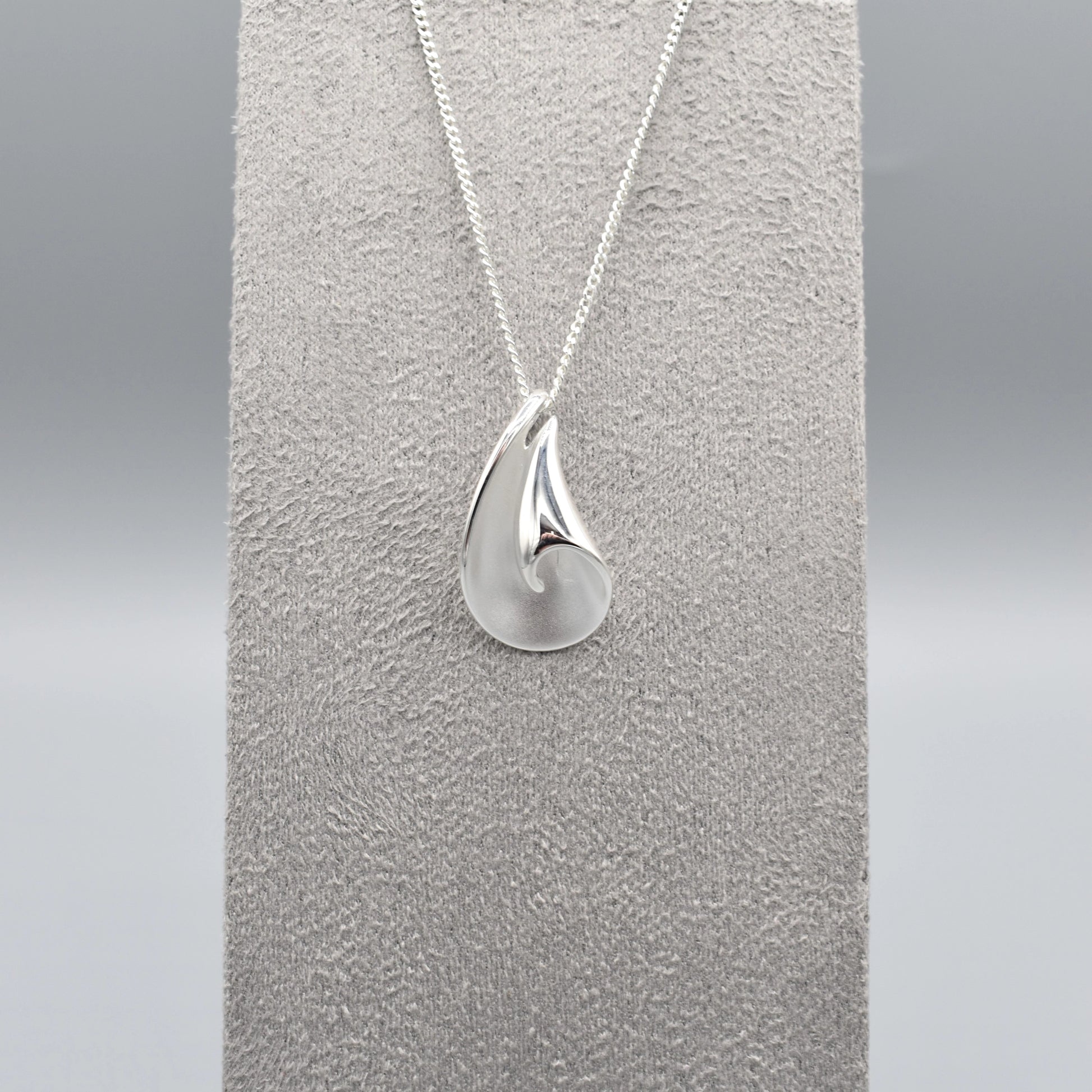A curved pendant with a twist in a matt and polished silver finish on a silver chain