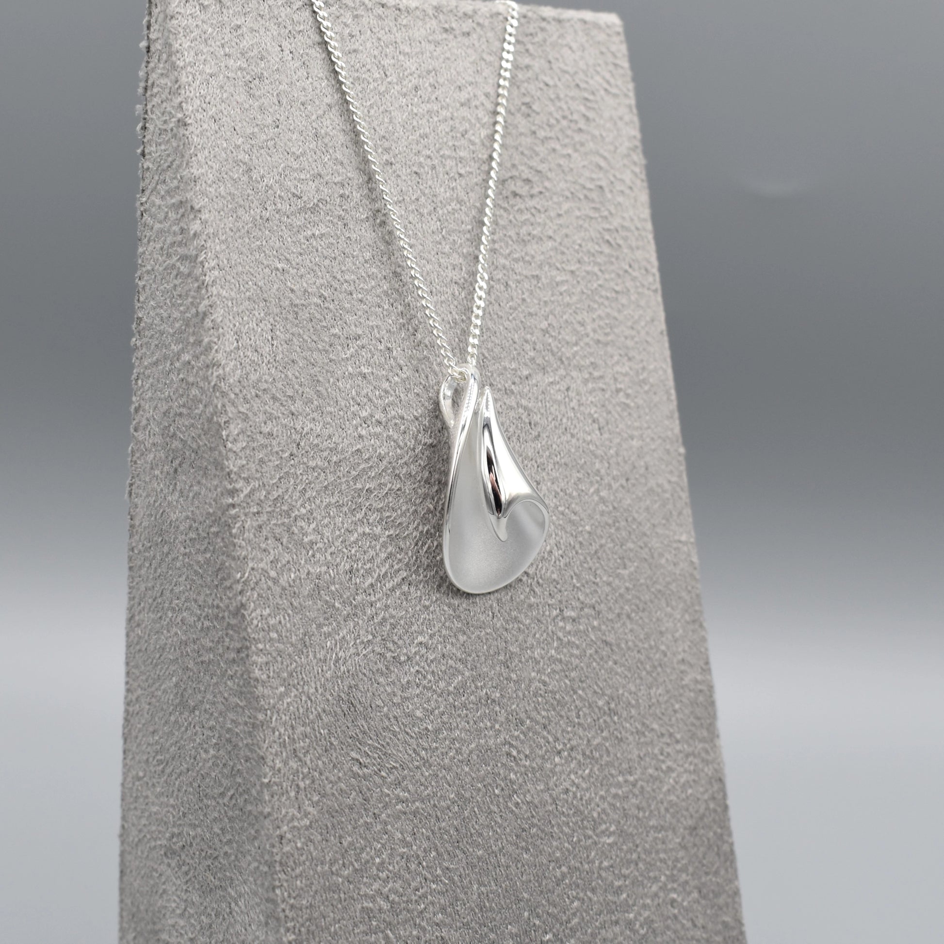 A curved pendant with a twist in a matt and polished silver finish on a silver chain side view