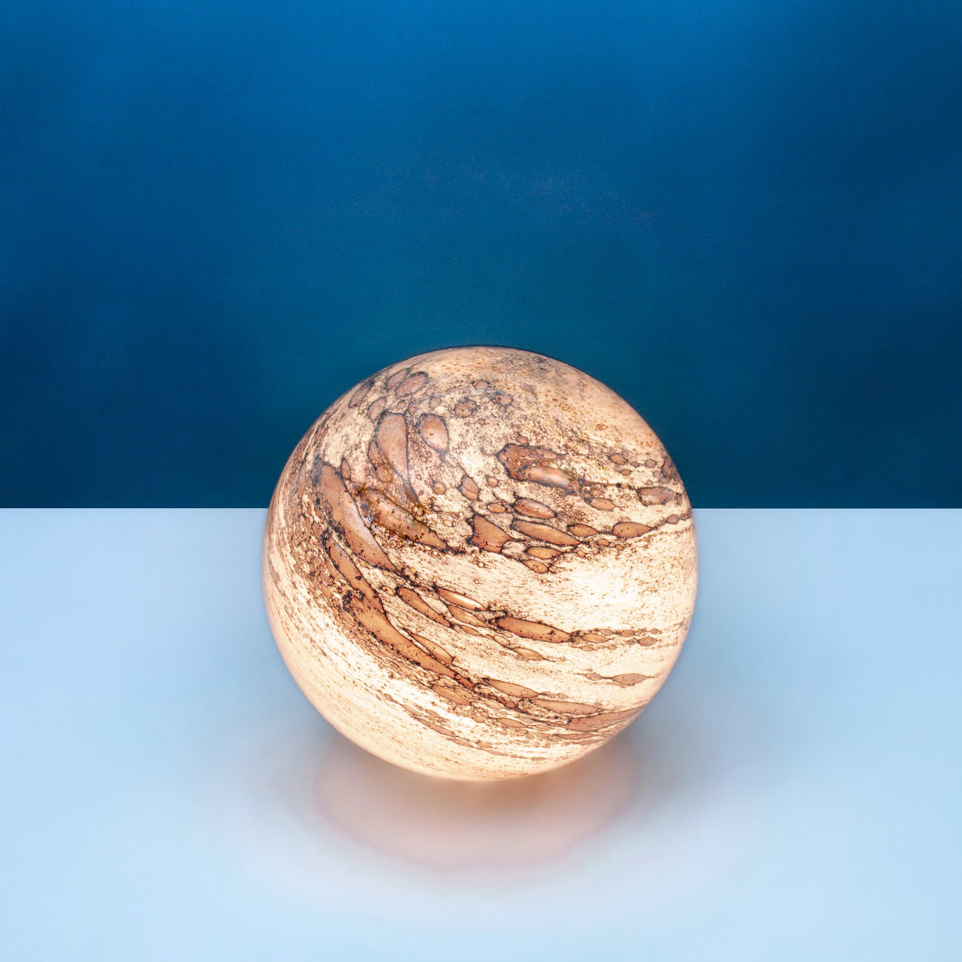 Round glass table light with a design based on the planet mercury and a warm light