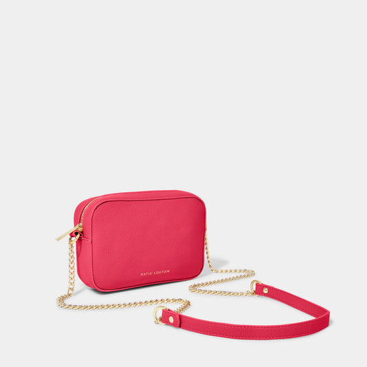 A fuchsia camera bag with gold chain detail on the strap, textured leather and a zip top