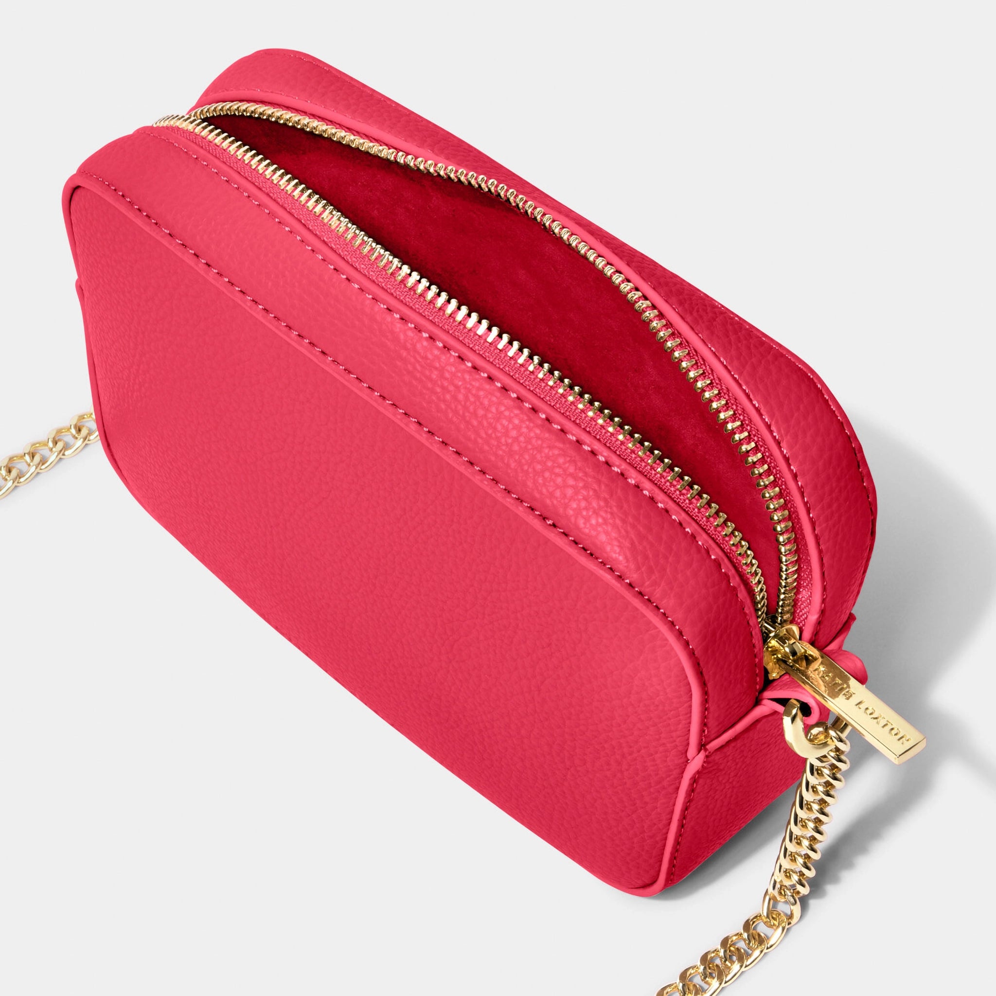An open fuchsia camera bag with gold chain detail on the strap, textured leather and a zip top
