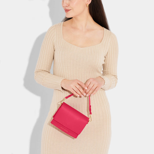 Model wearing pink crossbody bag with carry handle and belt buckle style shoulder strap