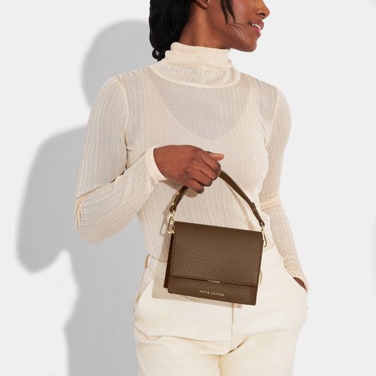 Model wearing brown crossbody bag with carry handle and belt buckle style shoulder strap