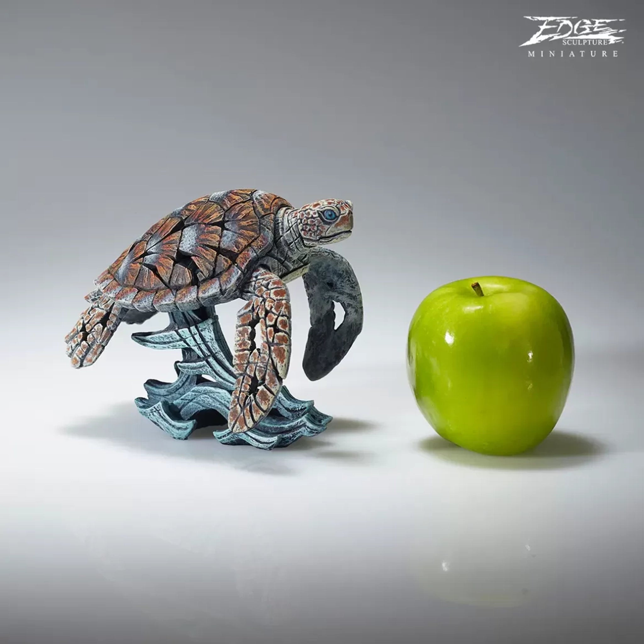 A textured and painted sea turtle surfing waves sculpture size comparison with apple