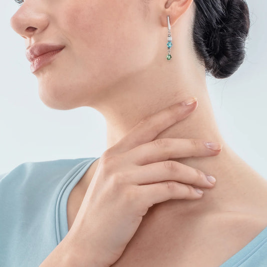 Model wearing a pair of drop earrings featuring stainless steel with blue and green cut glass beads