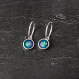 A pair of silver hoop earrings with round drops in blue and purple enamel
