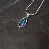 A teardrop shaped pendant with a silver frame and moon and purple and blue enamel