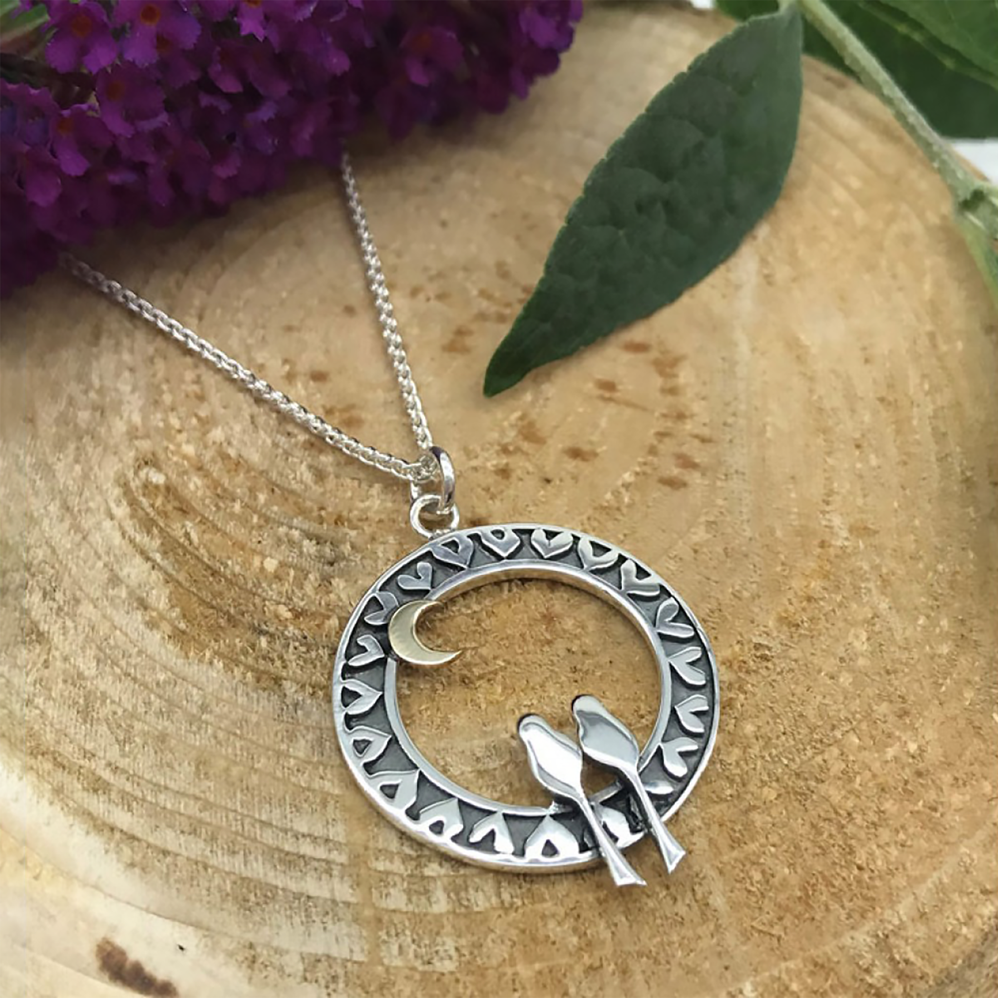 Posed silver pendant with two birds in a round heart decorated frame with a gold moon at the top, on a silver chain