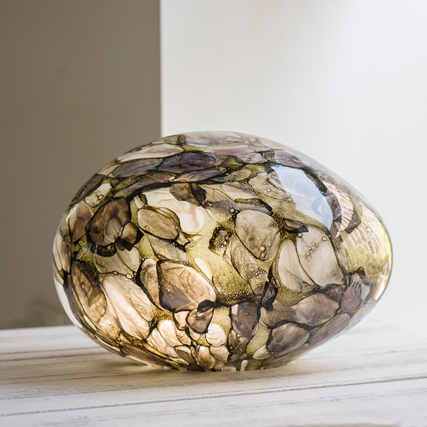 A pebble shaped glass lamp with a design based on sun dappled rivers