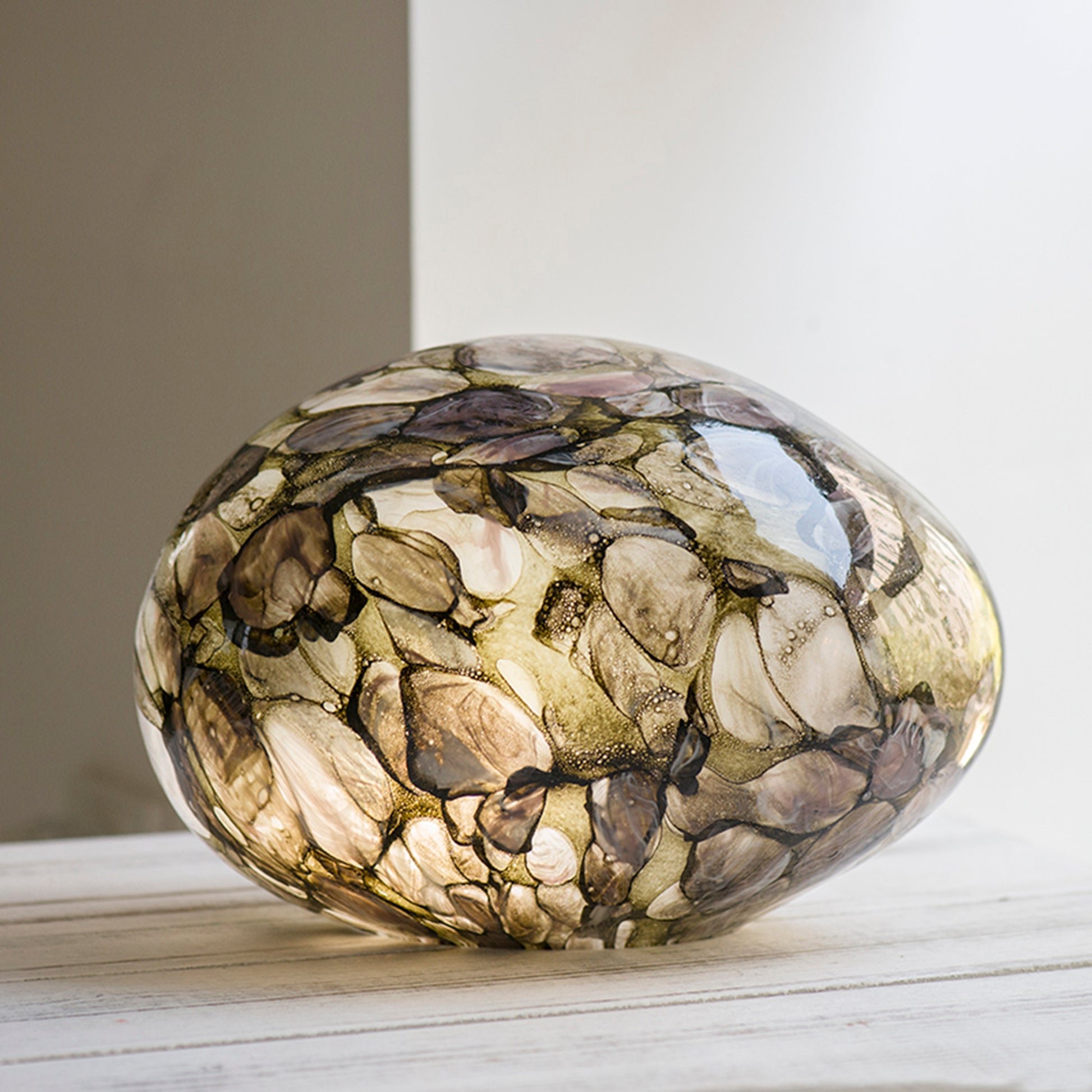 A pebble shaped glass lamp with a design based on sun dappled rivers