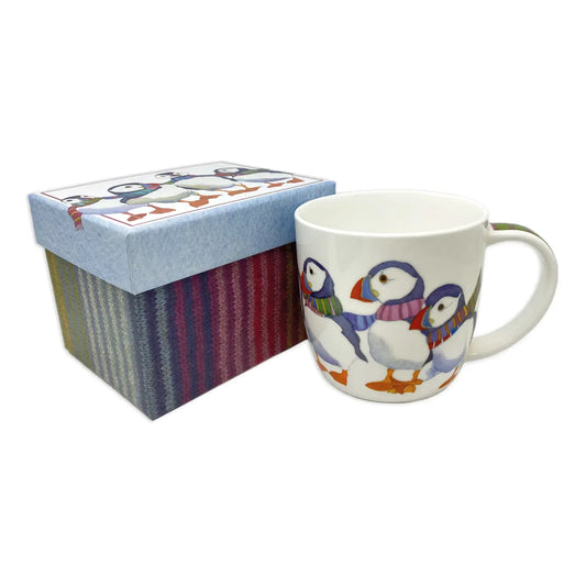 A white mug with an illustration of puffins in scarves next to a matching gift box