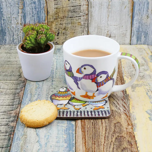 A white mug with an illustration of puffins in scarves with tea and a biscuit