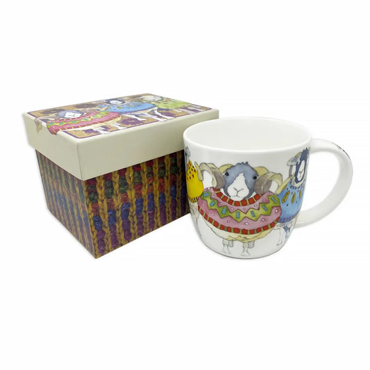 A mug featuring artwork with sheep in knitted sweaters, posed next to a matching packaging gift box
