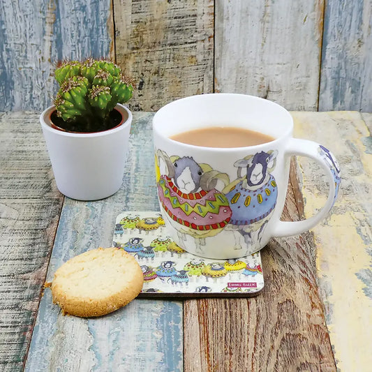 Mug with sheep in sweater design on a matching coasters staged with a biscuit