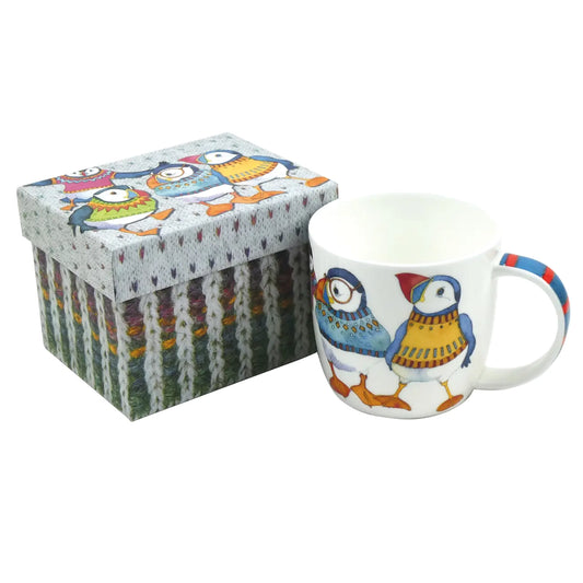 A white mug with an illustration of puffin in woolly jumpers next to a matching gift box