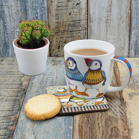 A white mug with an illustration of puffin in woolly jumpers with tea and a biscuit