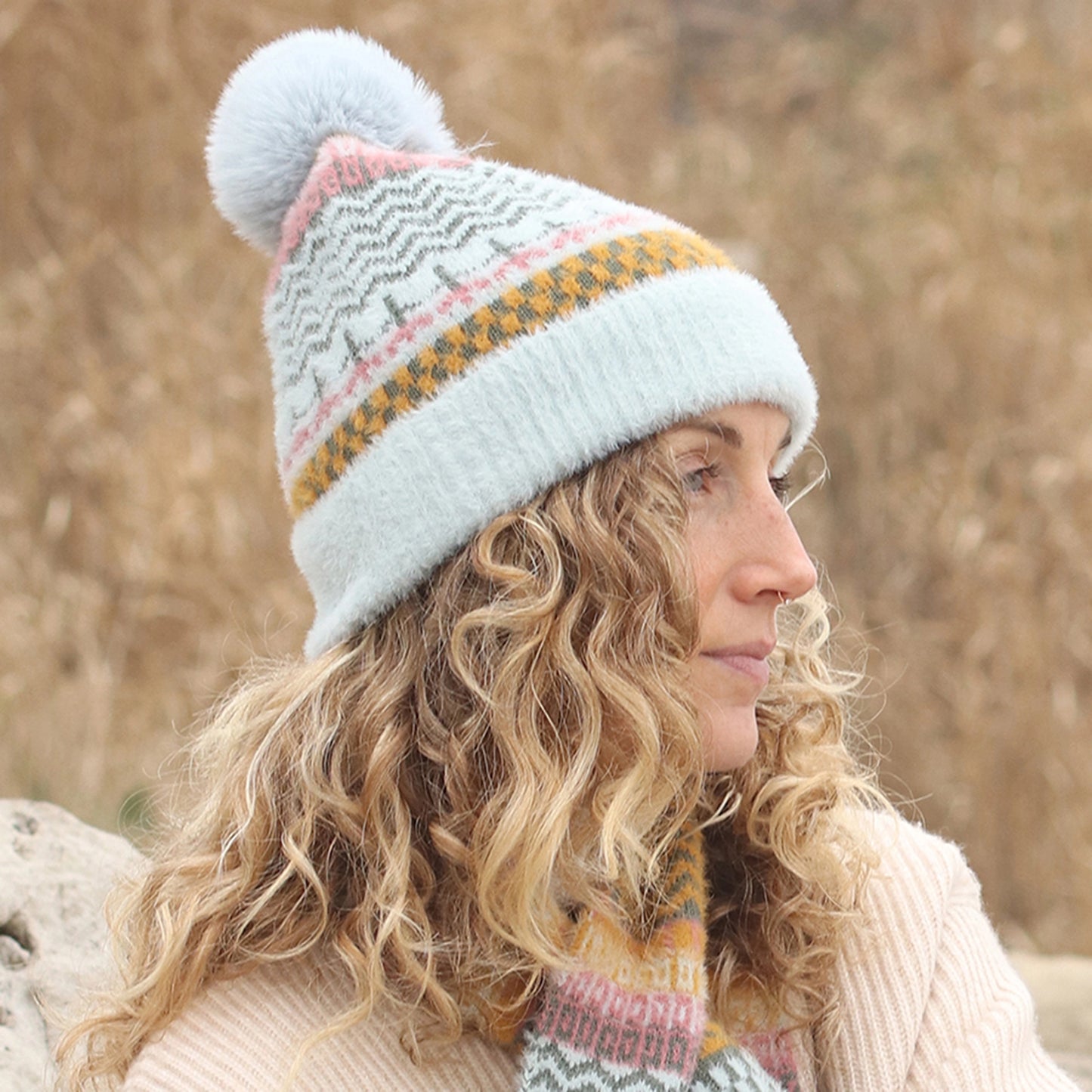 Model wearing multi patterned brushed knitted hat with faux fur pompom in aqua, pink and yellow
