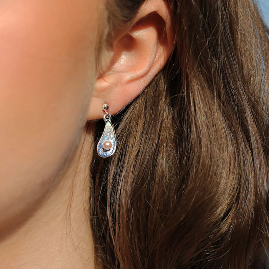 Model wearing a mussel shaped earrings with blue enamel and a white pearl