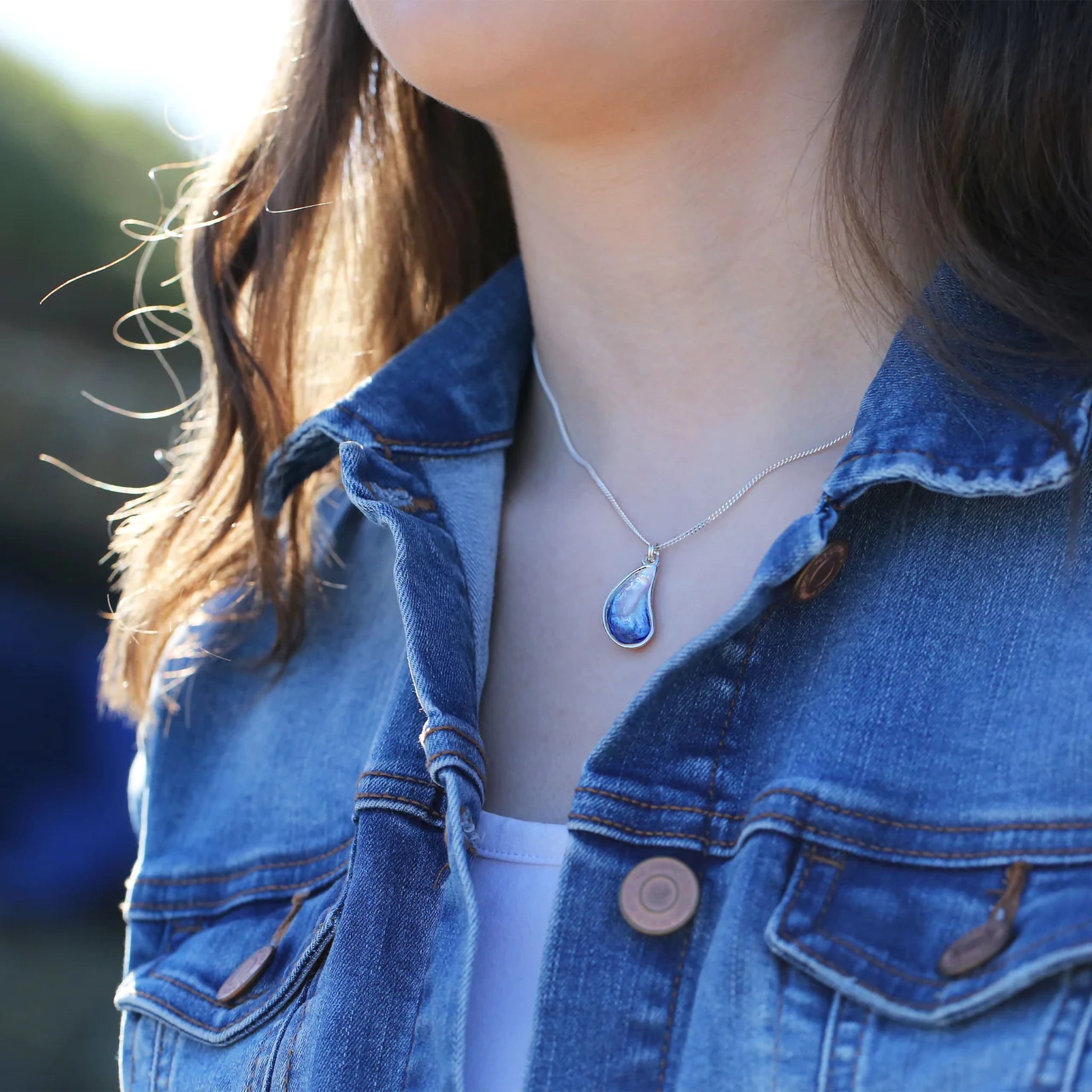 Model wearing silver pendant in the shape of a mussel with a pearly white and blue enamel, on a silver chain