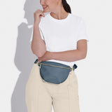 Model wearing a belt bag in faux leather and navy blue with gold hardware
