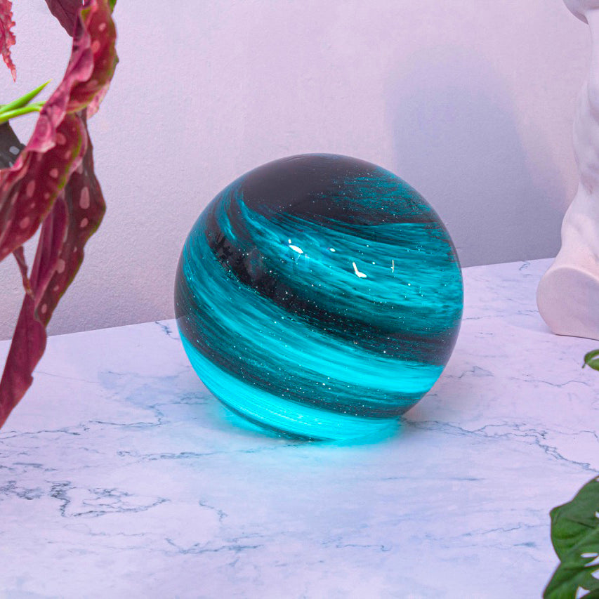 A round glass orb lamp designed based on the planet Neptune in swirls of lights and dark blue lifestyle