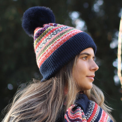 Model wearing knitted Nordic stripe pattern hat in blue, green and rust colours with faux fur pompom