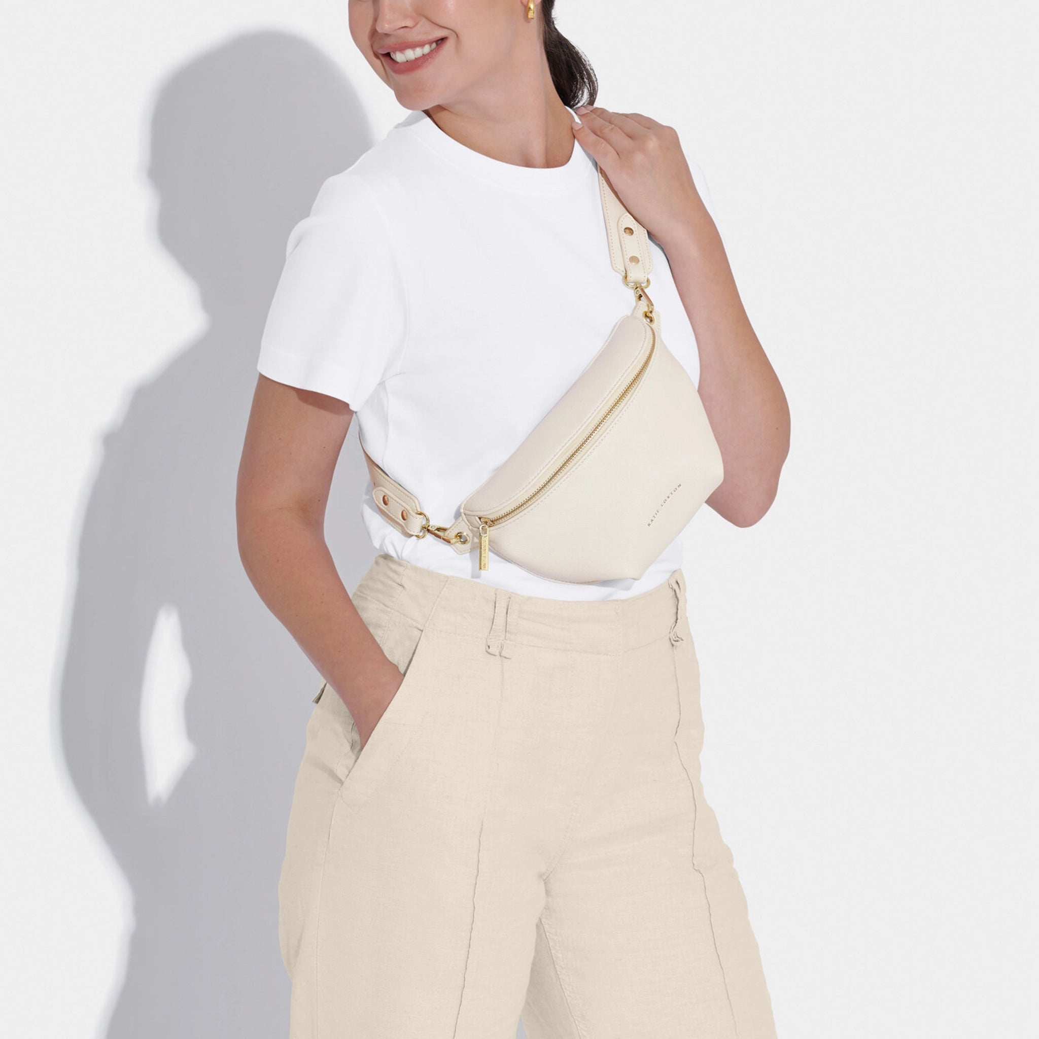 Model wearing a belt bag in faux leather and off-white with gold hardware