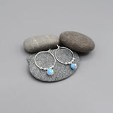 A pair of silver hoop earrings with round silver beads and blue opalique drops