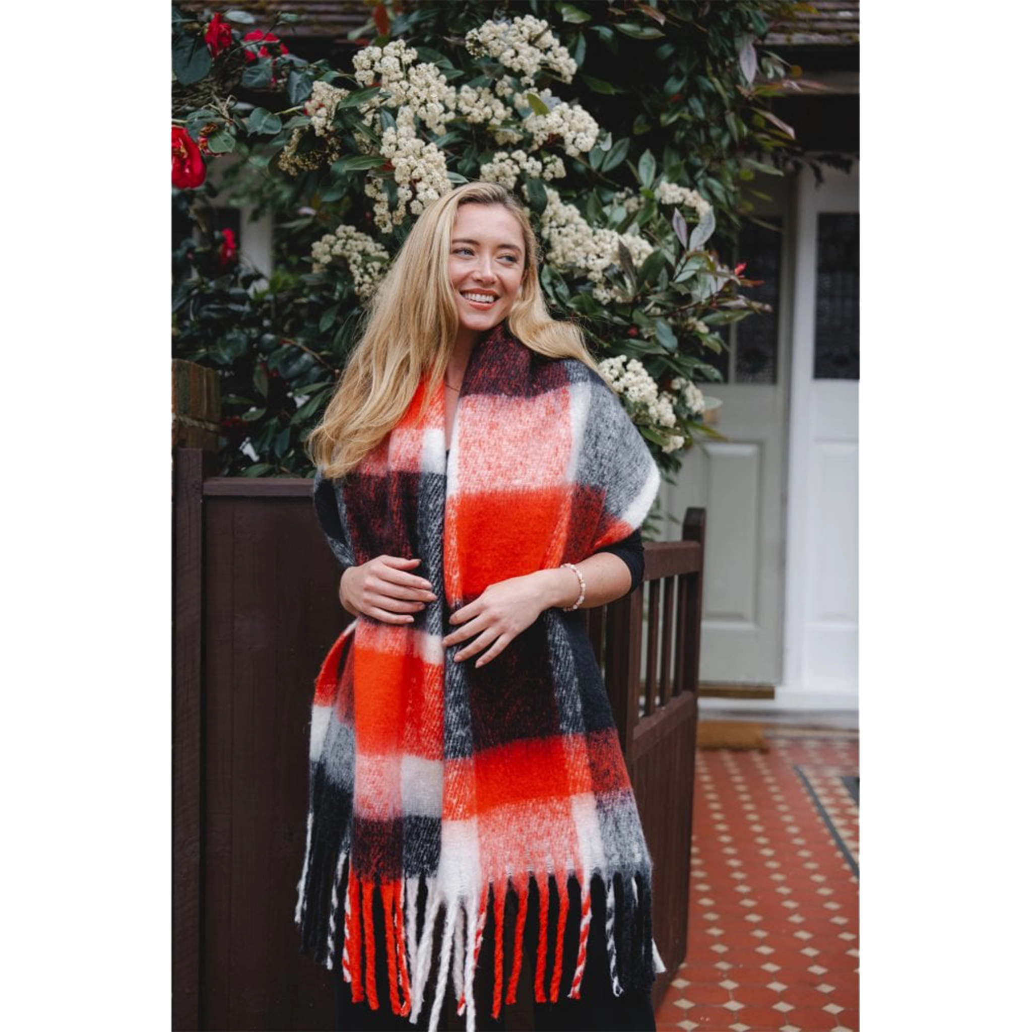 Model wearing a chunky knit black and orange check patterned scarf with tassel trim