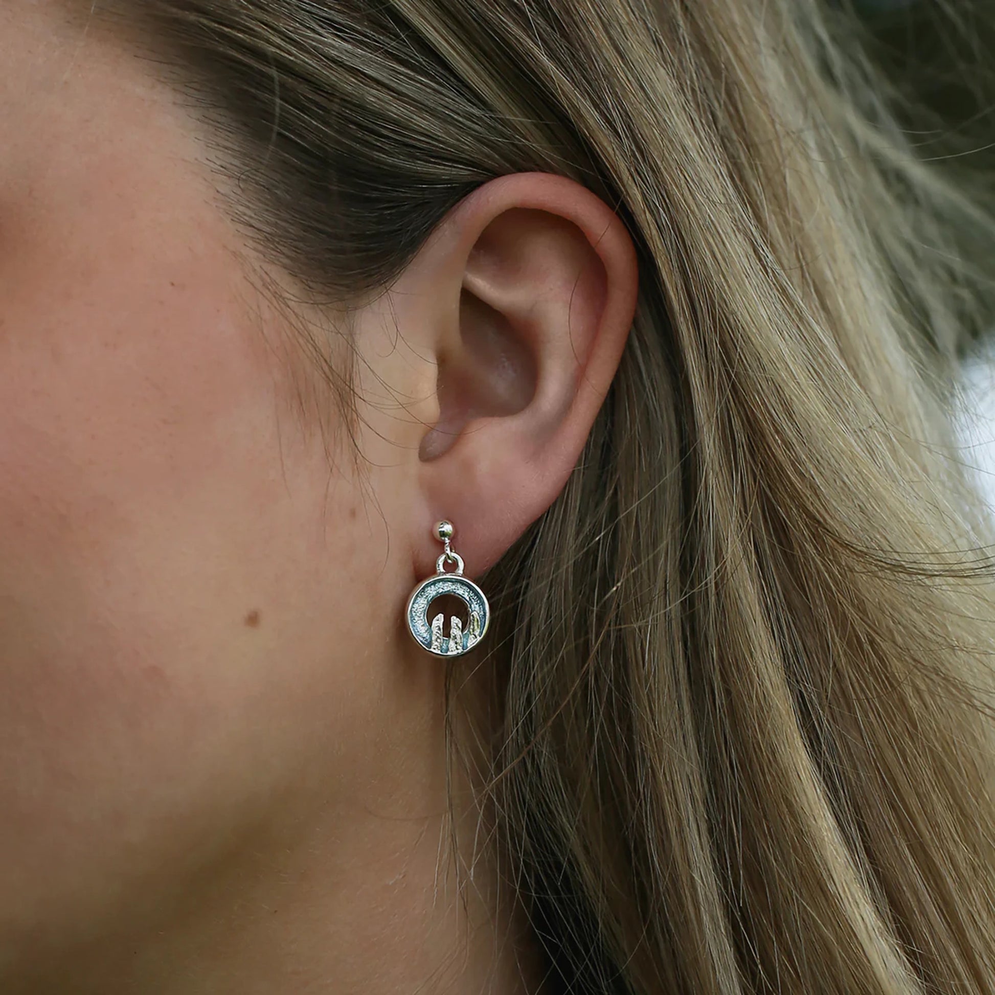 Model wearing silver drop earrings with round open circles in blue grey enamel, finished with a standing stone design