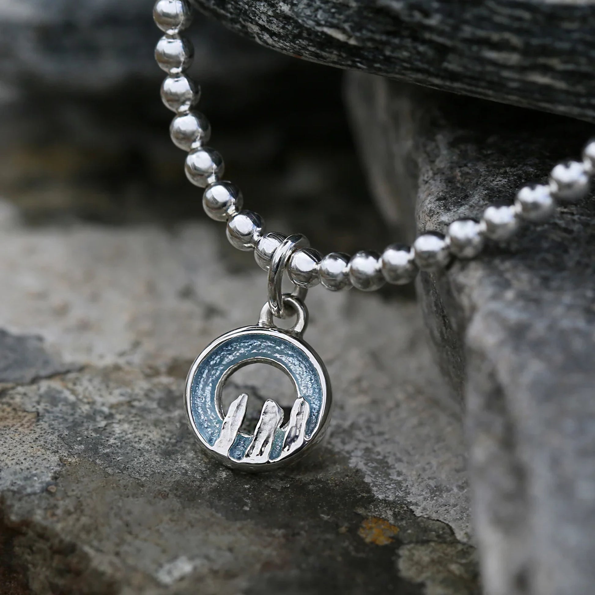 Silver stretch bracelet with a round blue grey enamelled charm with standing stone design - lifestyle