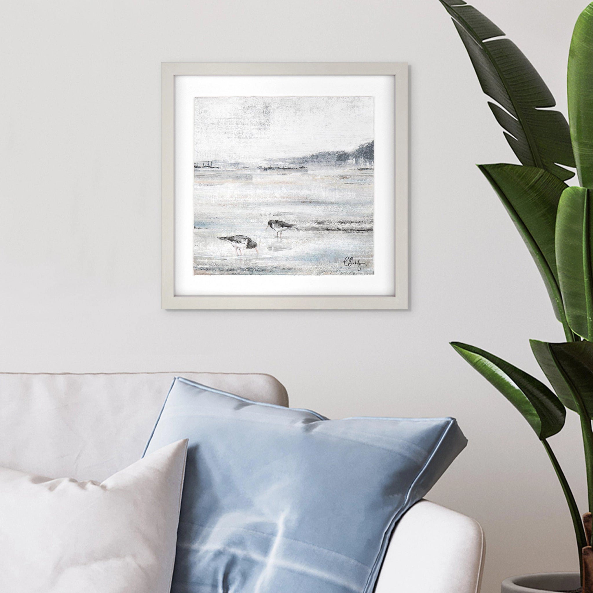 Framed print of oyster catcher birds on a sandy beach at low tide in wispy greys and blues hanging in a light room.