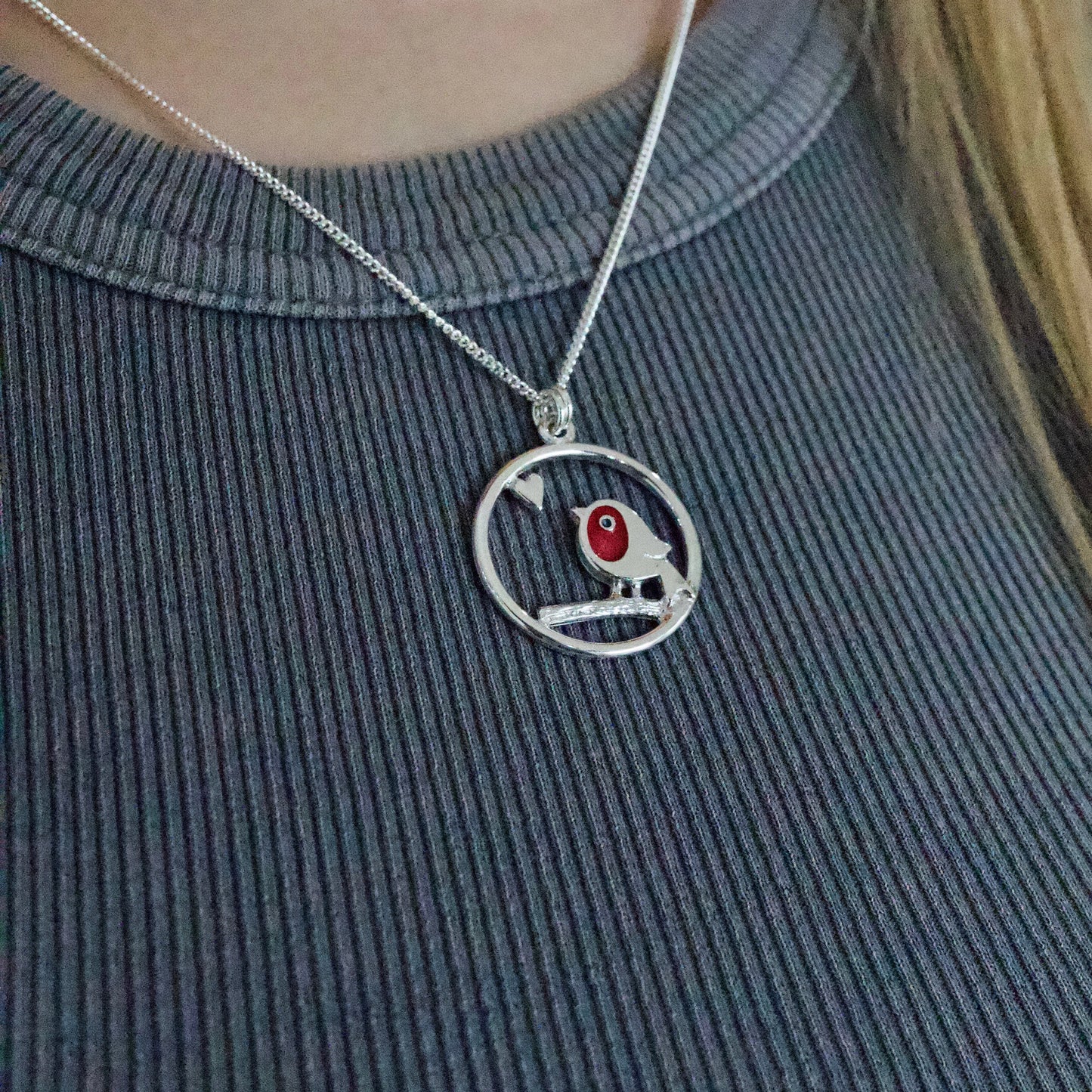 Model wearing silver pendant with framed red enamel robin and heart detail on silver chain