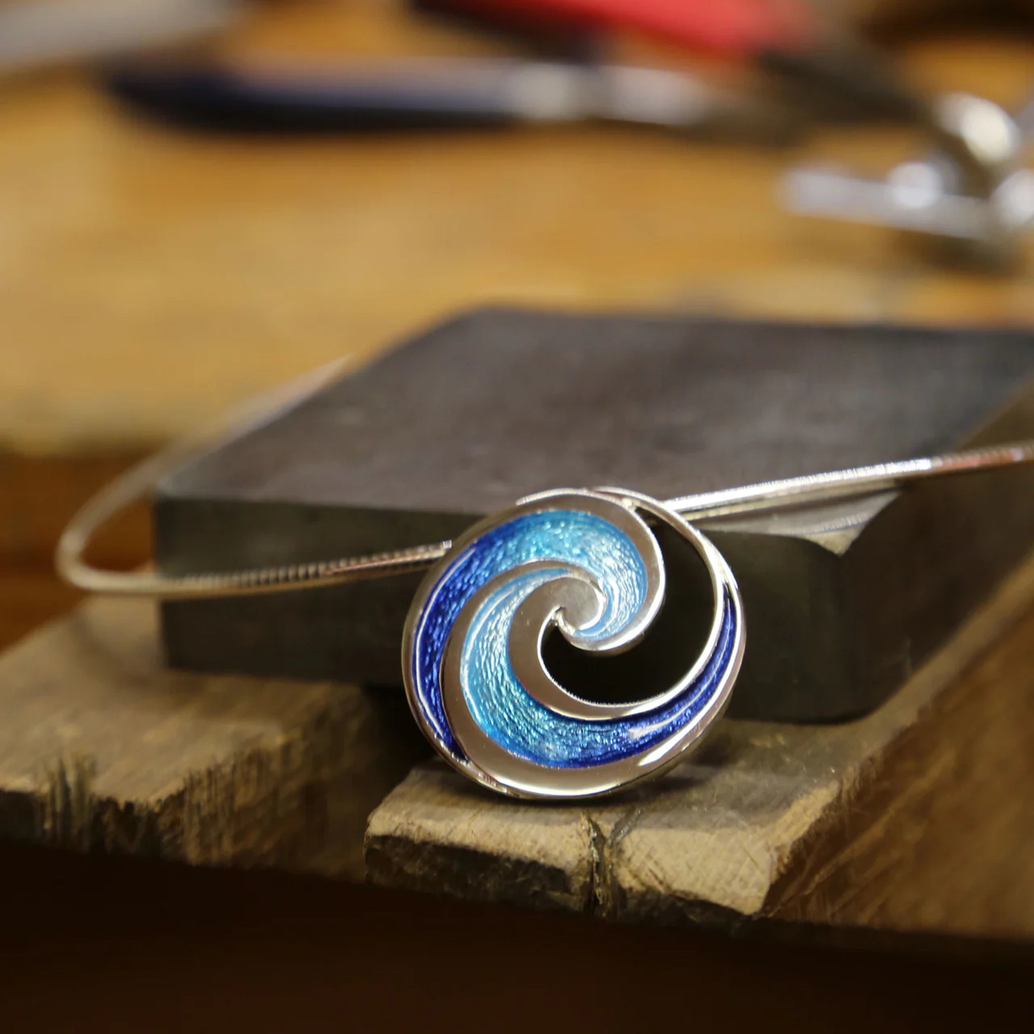Silver necklet with large round pendant featuring blue enamel ocean wave design on neck wire