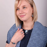 Model wearing silver necklet with large round pendant featuring blue enamel ocean wave design and matching peices