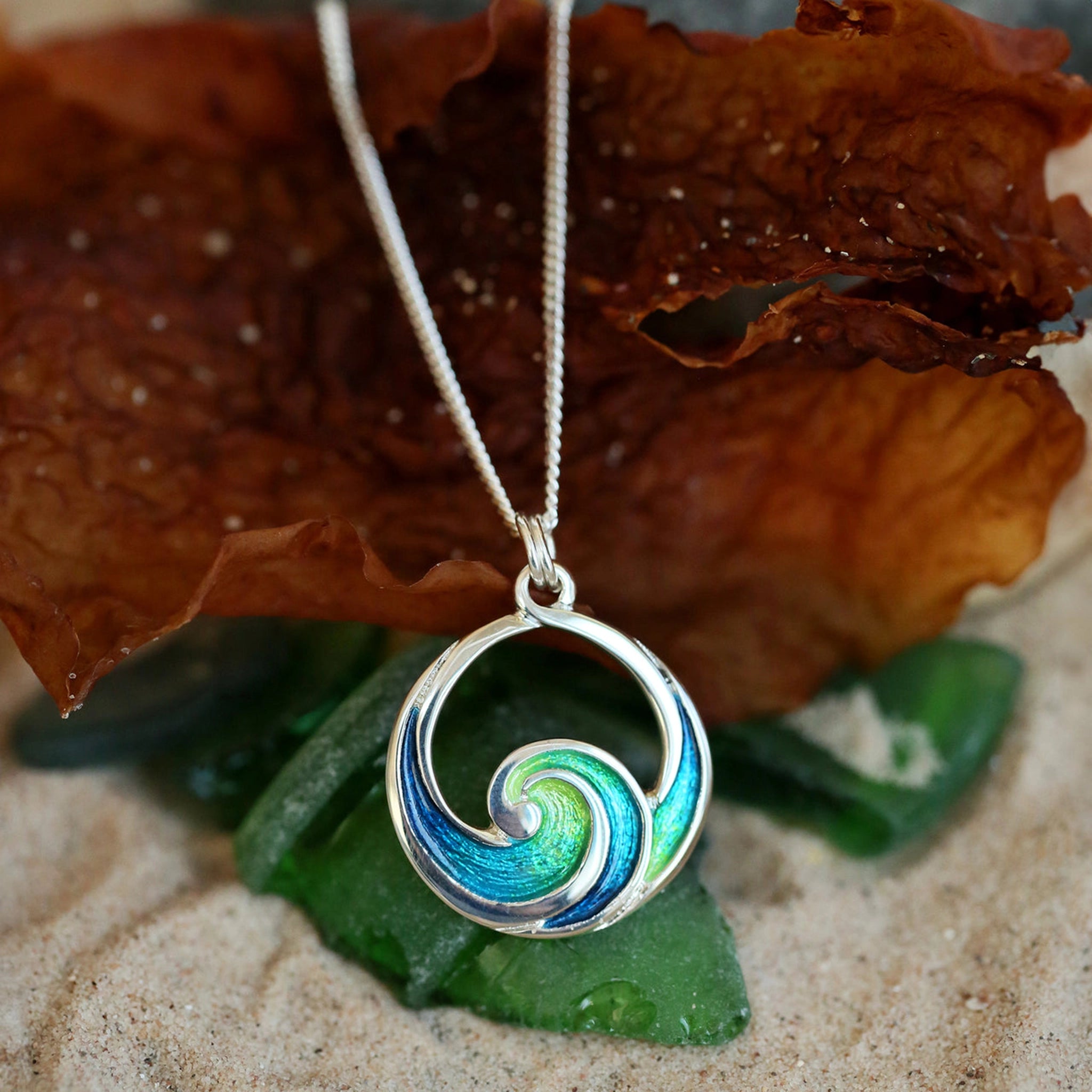 A silver pendant in the shape of an ocean wave coloured with blue and green enamel lifestyle image