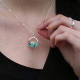 Model wearing a silver pendant in the shape of an ocean wave coloured with blue and green enamel