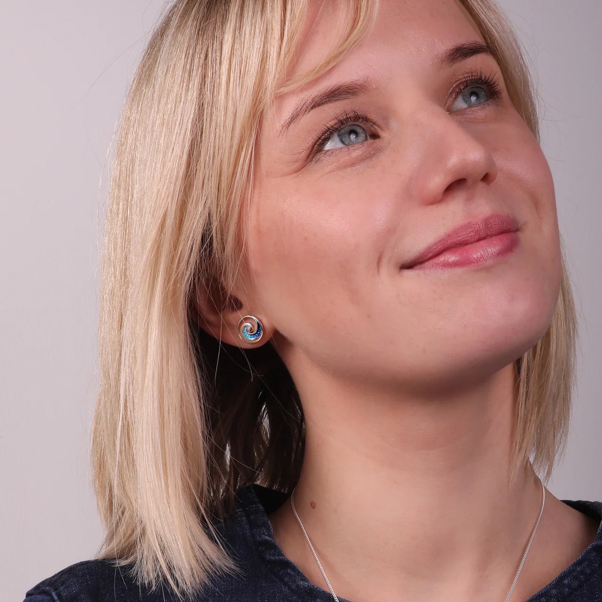 Model wearing polished silver round stud earrings with ocean wave design in blue enamel