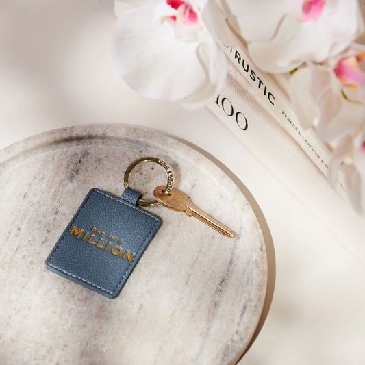 A faux leather navy keyring featuring the words One in a Million' in gold lettering with attached key