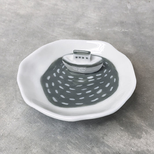 A white ceramic trinket dish with grey water design and a little boat