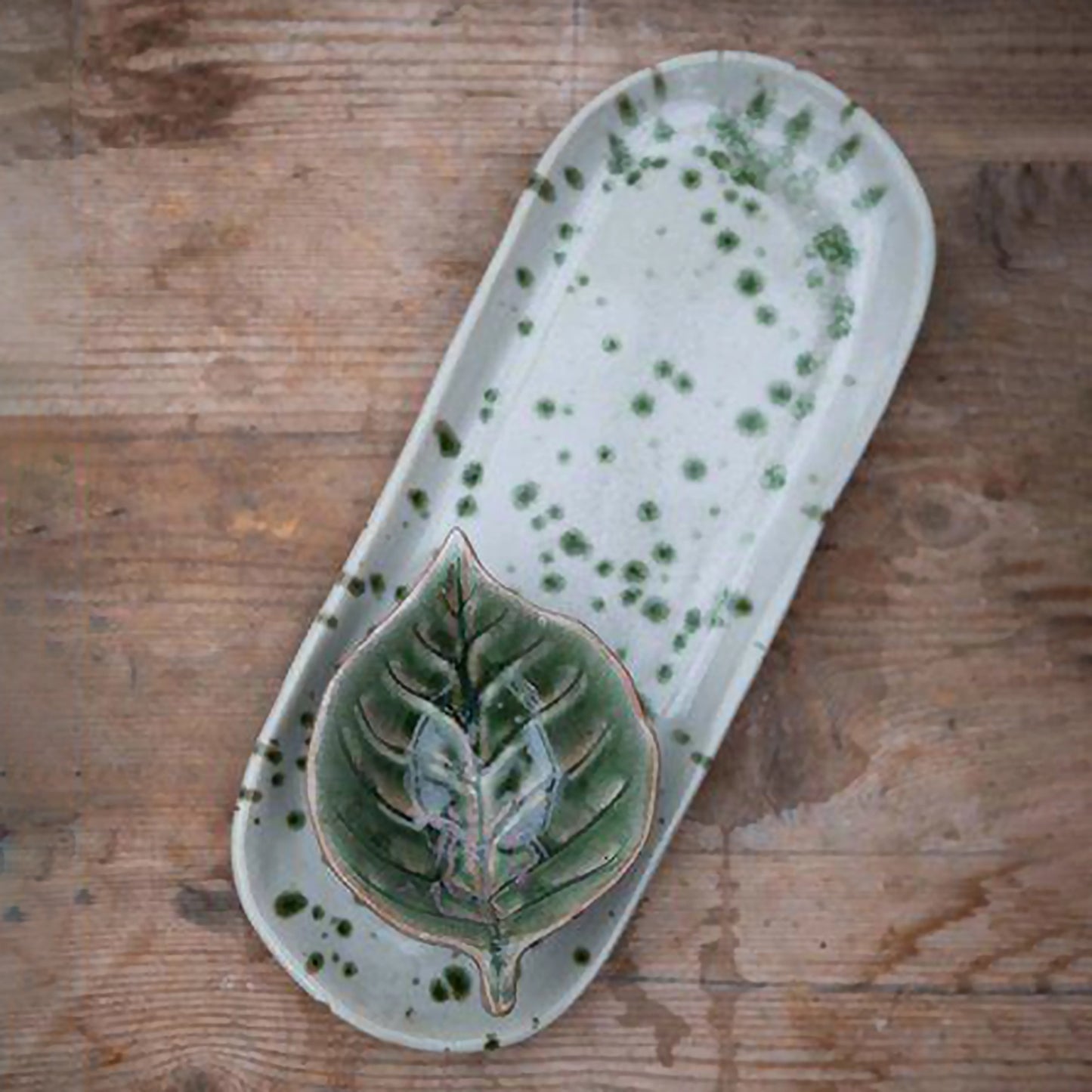 A long rounded plate in off-white with a green splatter pattern lifestyle