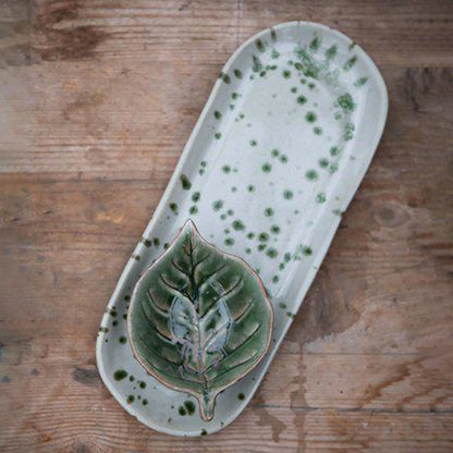 A long rounded plate in off-white with a green splatter pattern lifestyle