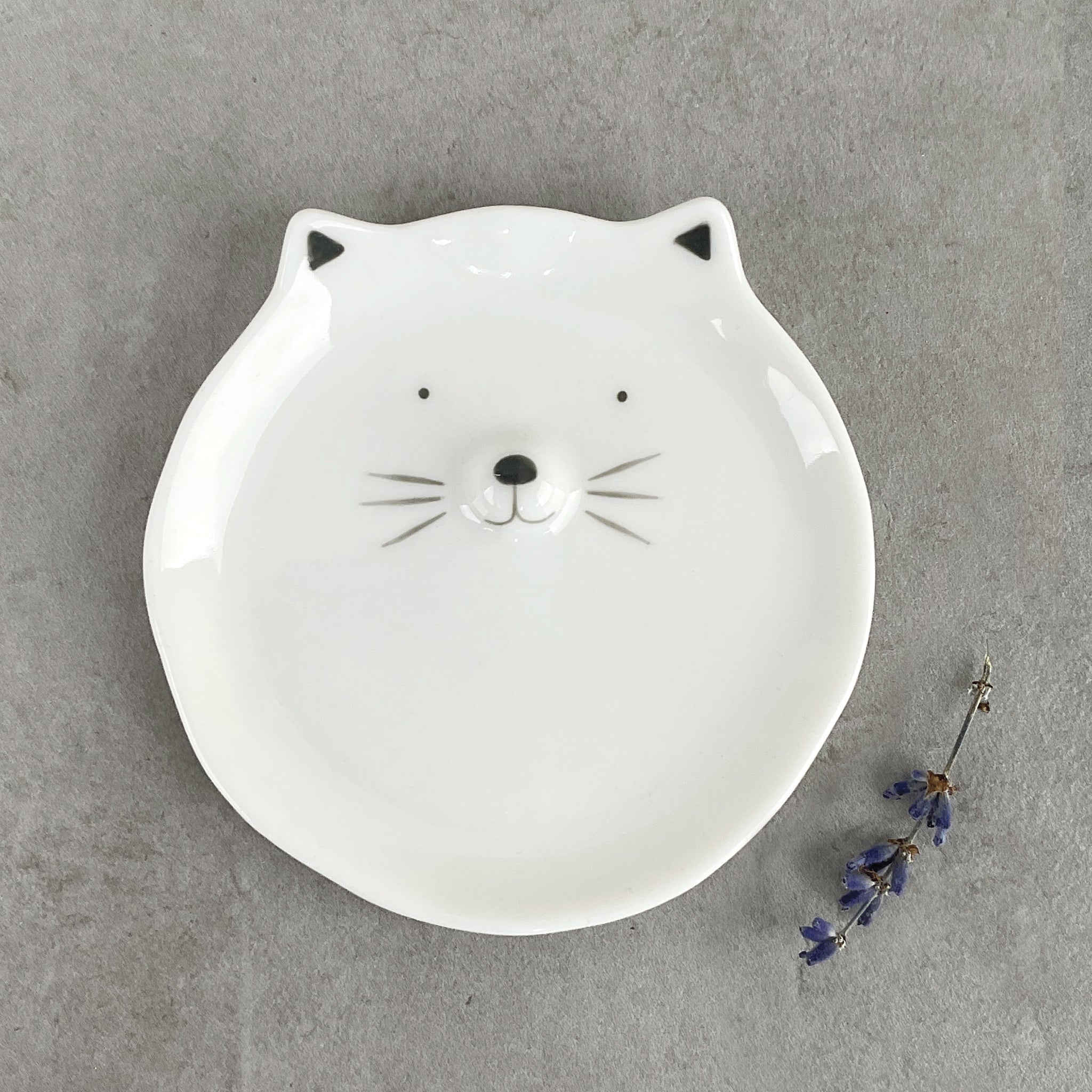 A round white ceramic trinket dish with a cat face and ears