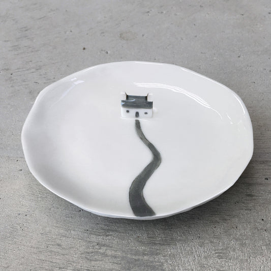 A ceramic white dish featuring a little cottage and a path