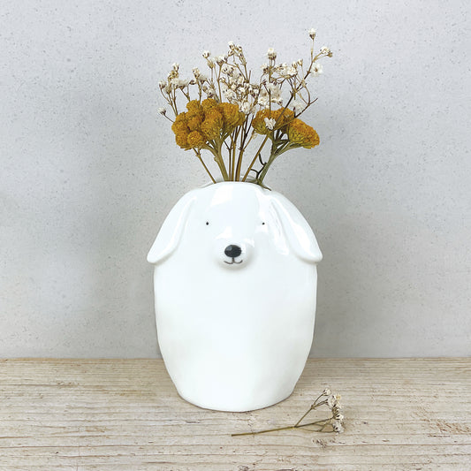 A minimalist white vase shaped like a dog with some dried flowers