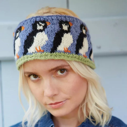 Model wearing knitted headband in blue featuring a design of a row of Puffins with beaded eyes