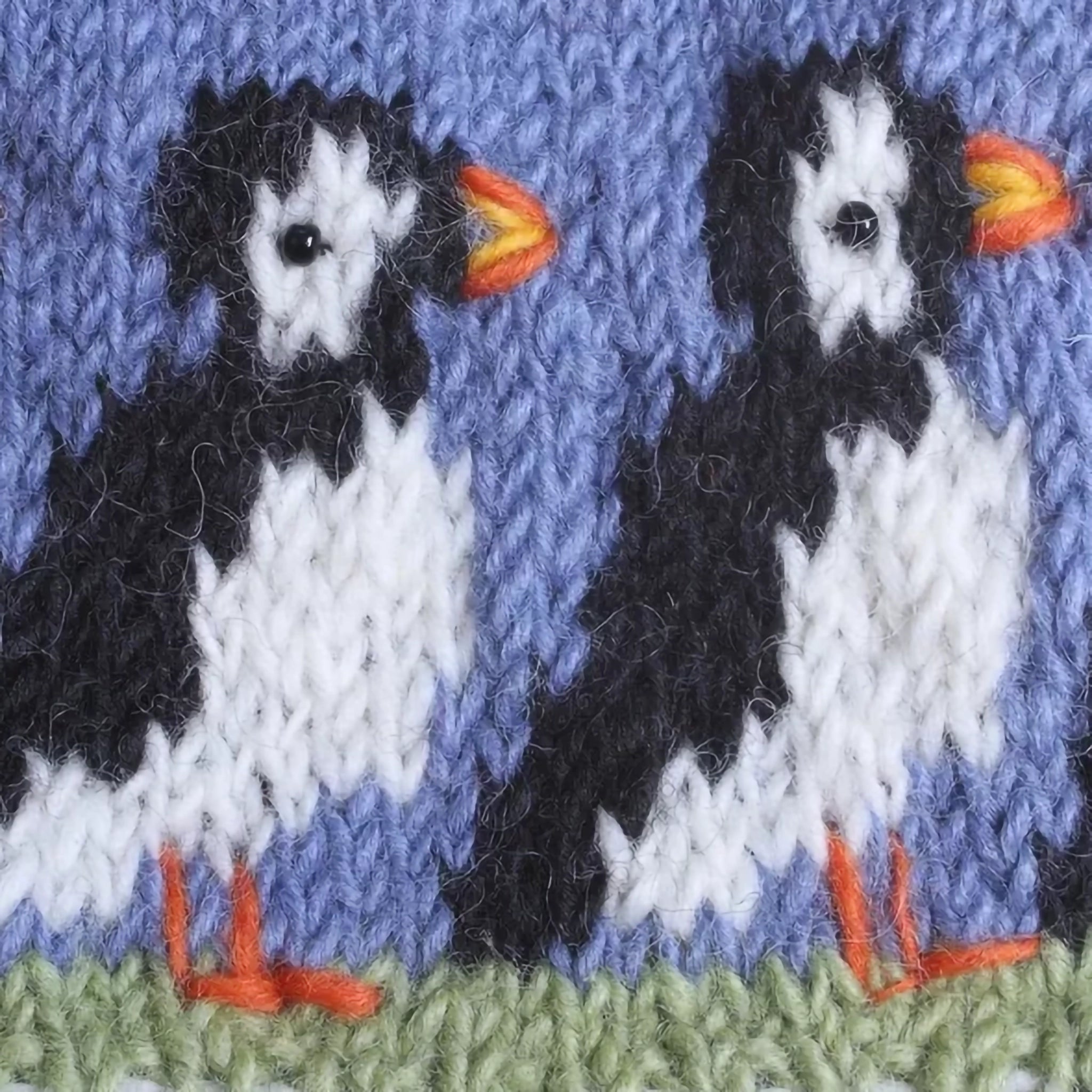 A knitted tea cosy with a pompom and a row of puffins design with beaded eyes detail