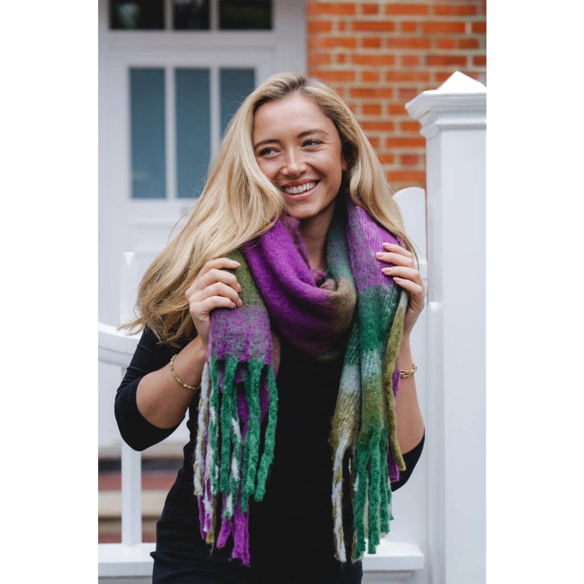 Model wearing a chunky knit purple, blue and green check patterned scarf with tassel trim