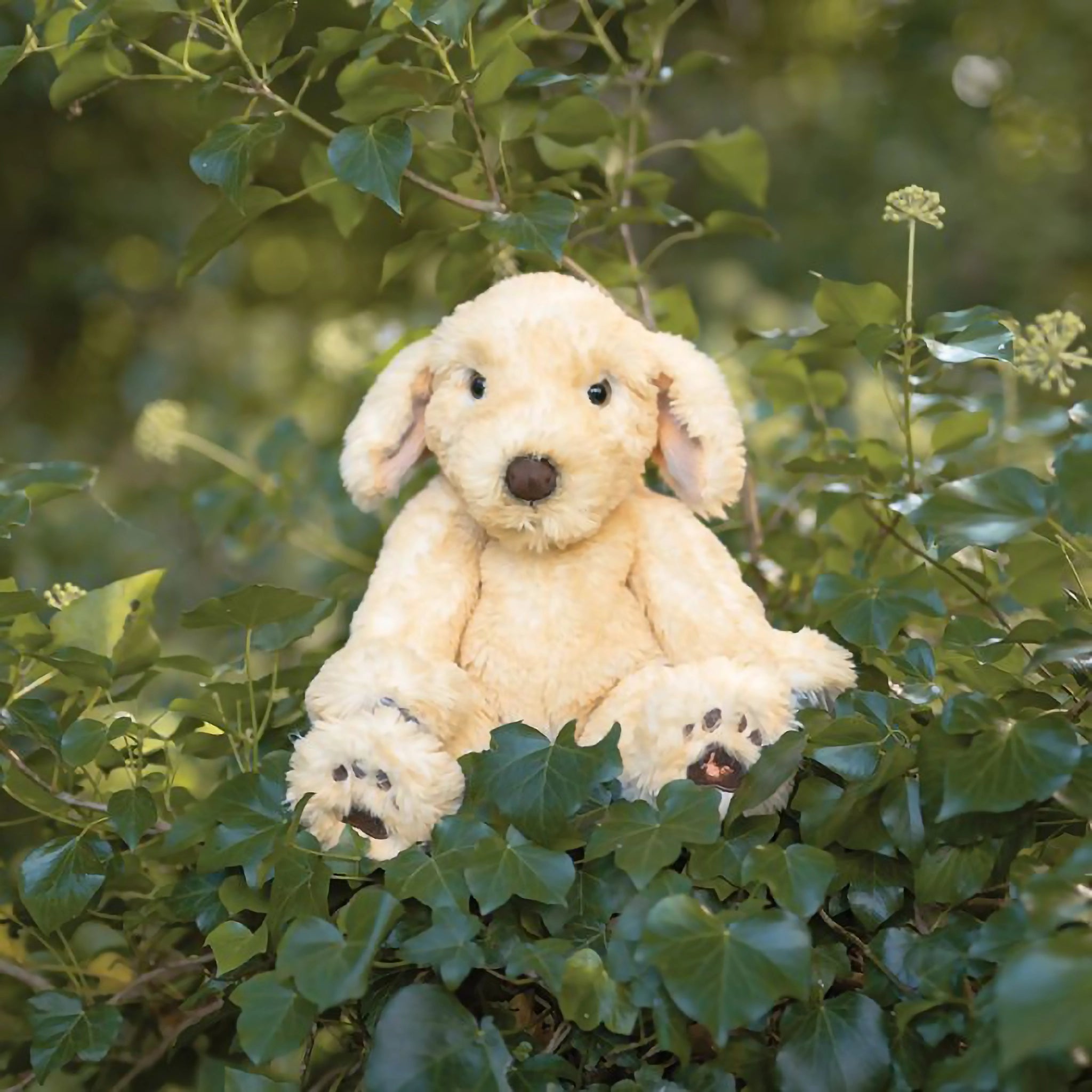 A stuffed labrador puppy plush toy with the Wrendale logo embroidered on the bottom of its foot posed in ivy